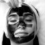 A woman with closed eyes receives a black facial mask, showcasing a relaxing facial in Nassau County, NY.