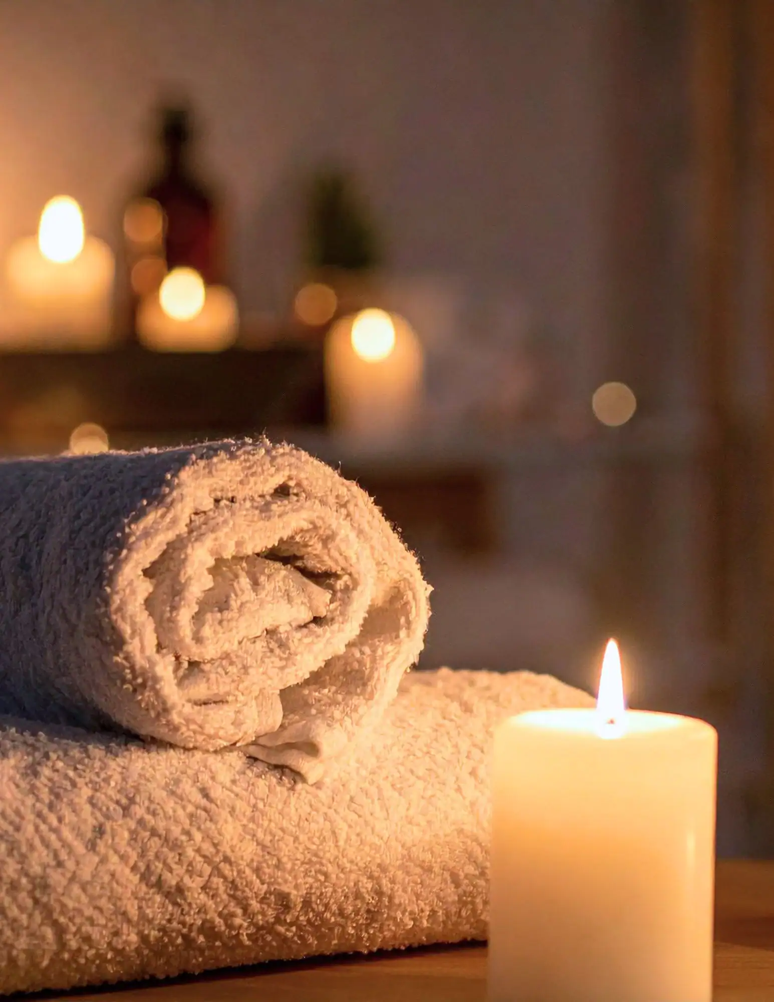Rolled towels and a lit candle sit on a table, creating a peaceful Medical Spa Nassau County ambiance.