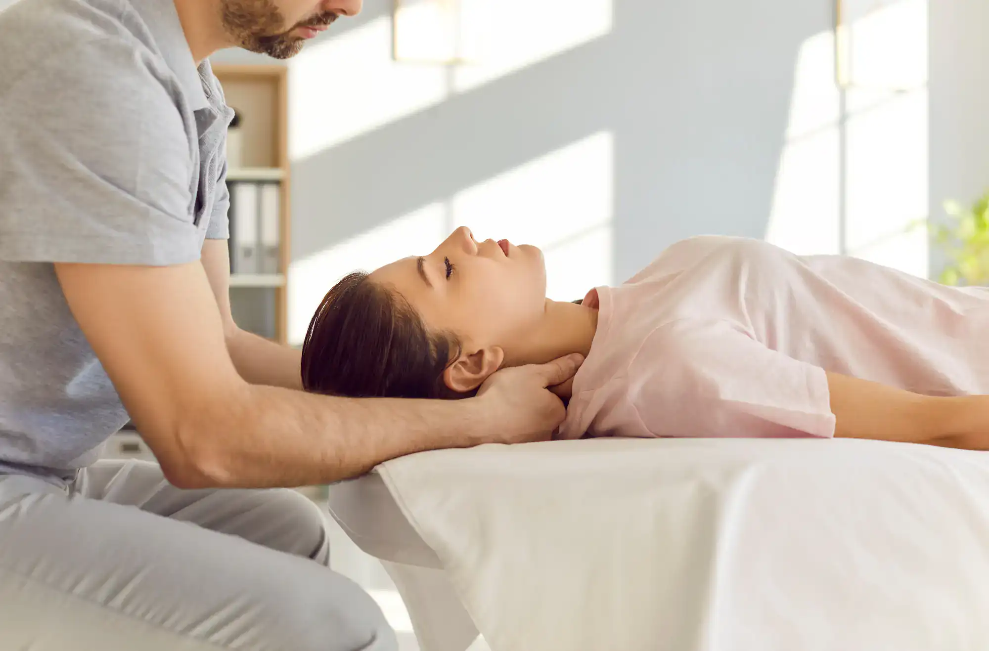 A person enjoys a relaxing neck and head massage on a massage table in a well-lit therapy room.