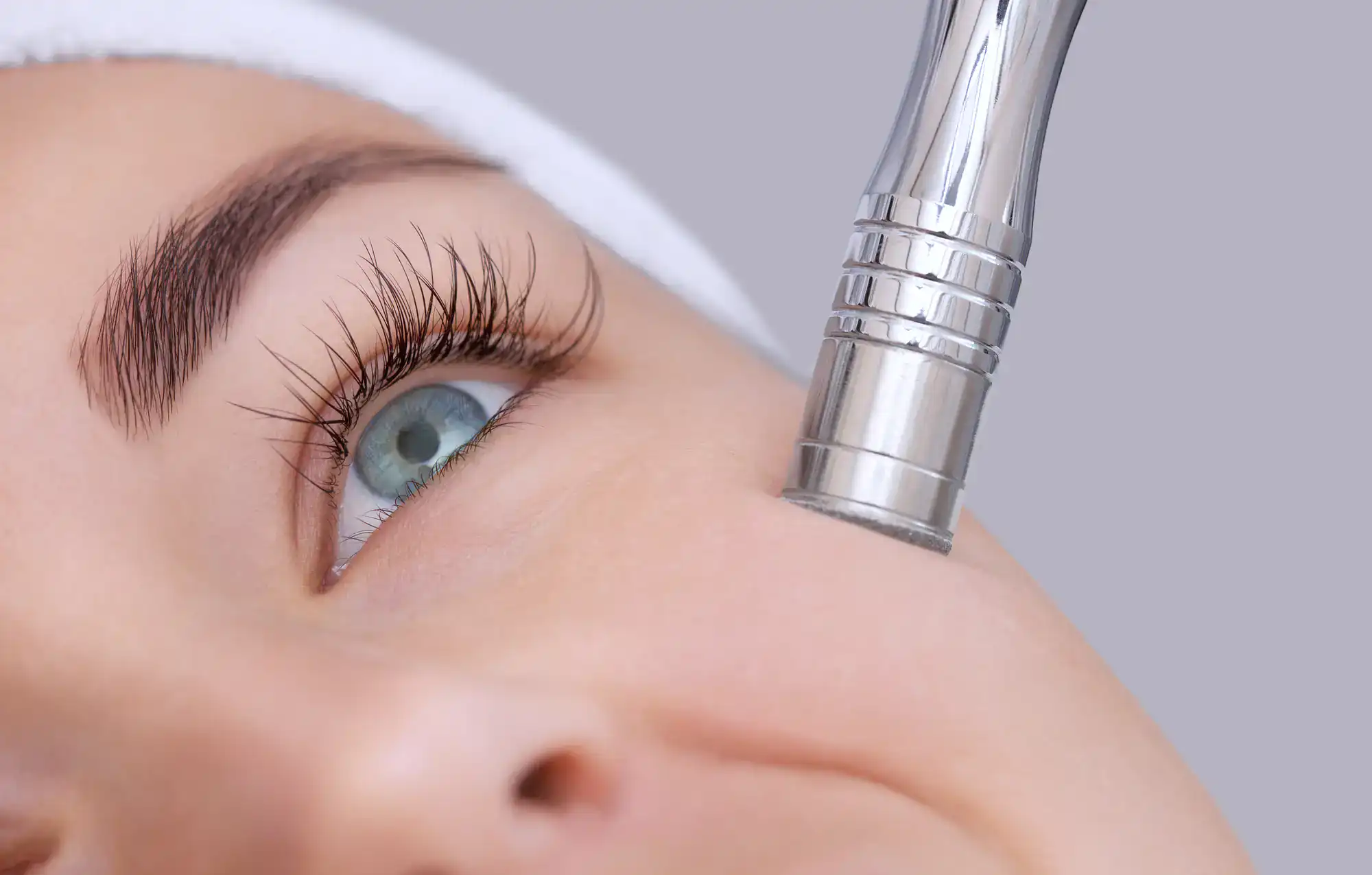A woman receives a facial treatment with a metal skin care device applied near her eye for rejuvenation.