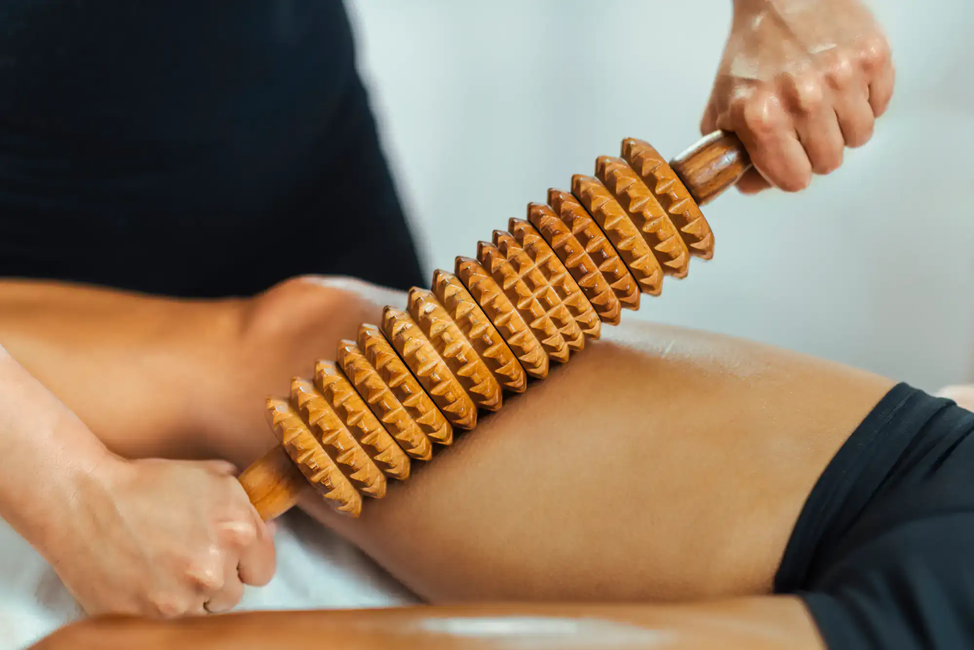 A person is using a wooden massage roller tool on another&rsquo;s thigh for muscle relief and relaxation therapy.