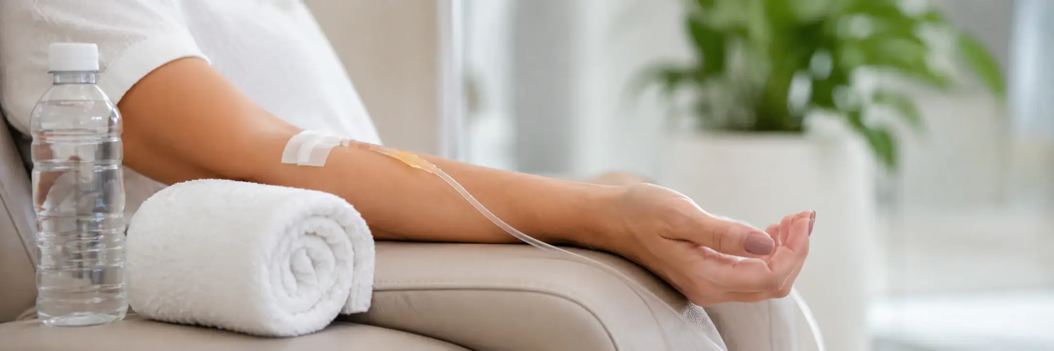 A patient receives IV therapy in a chair, with hydration from a water bottle and comfort from a rolled towel.