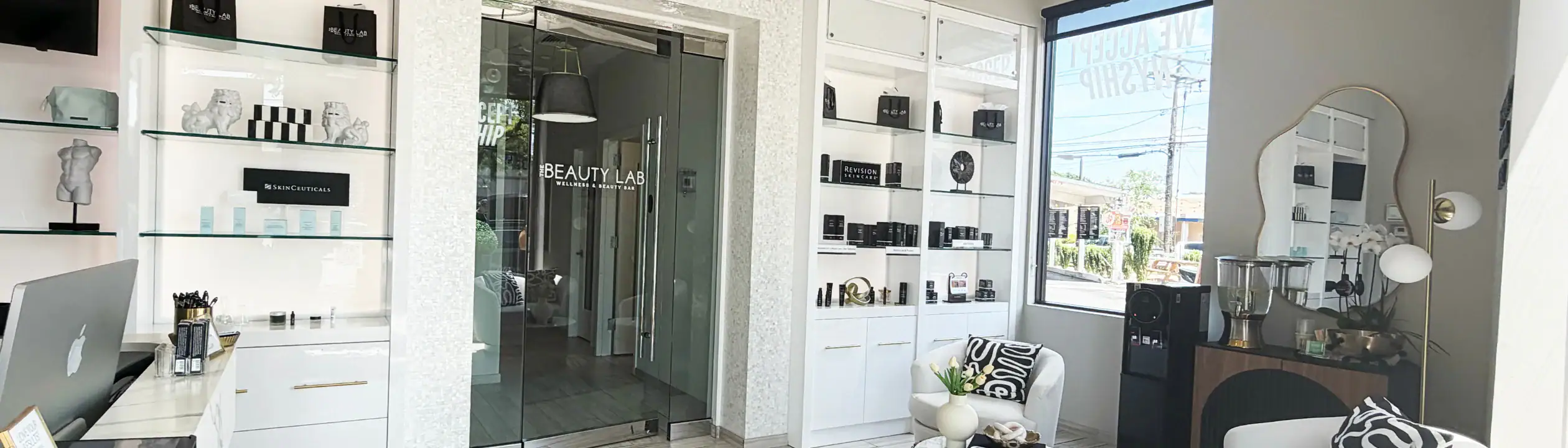 Modern beauty clinic lobby featuring product shelves, a glass door, window, and a stylish seating area.