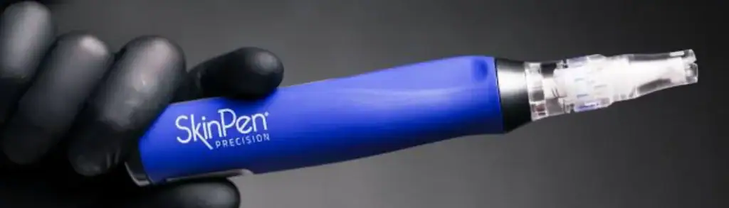 A gloved hand demonstrates the SkinPen Precision microneedling device, highlighting its blue color.