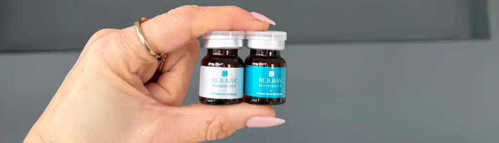 A hand with pink nails holds two Rejuvaskin Scar Esthetique vials against a gray background.