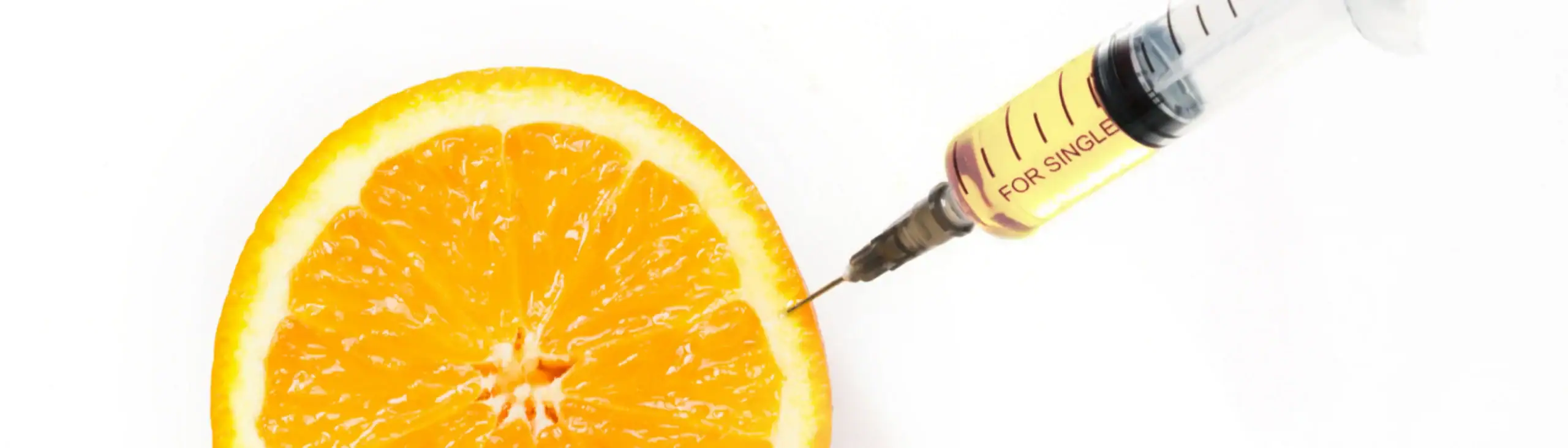 A syringe injecting liquid into a sliced orange on a white background, showing food injection technique.