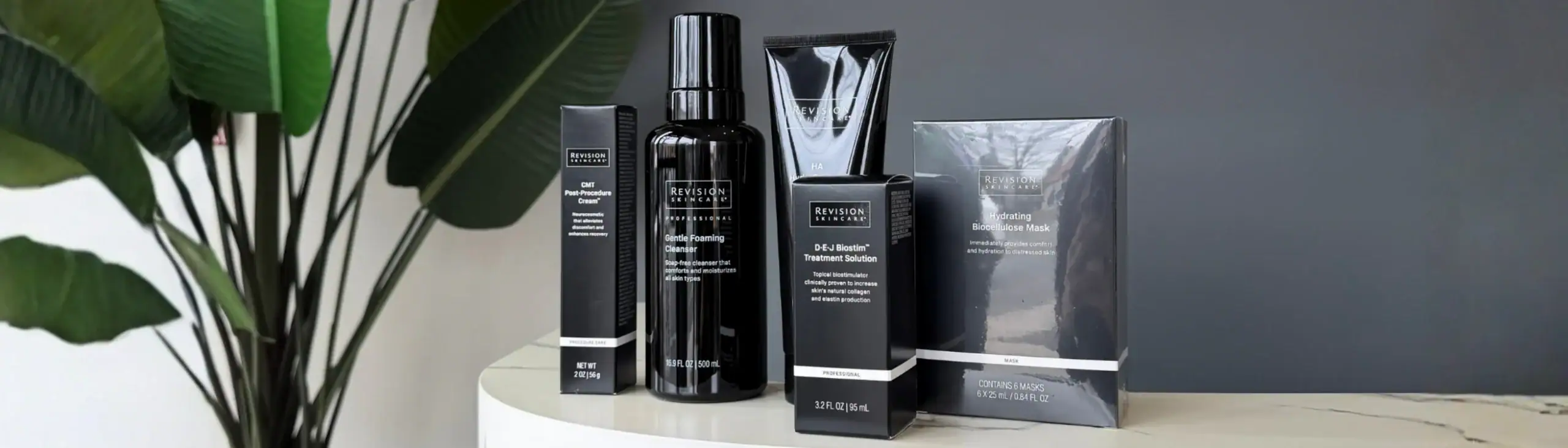 Five Revision Skincare products neatly arranged on a white countertop with a green plant in the background.